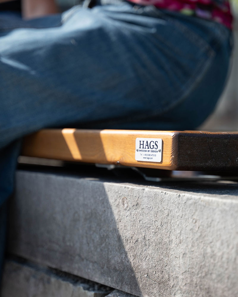 Close up of a person sitting on a HAGS bench, you can see the bench and the HAGS logo.